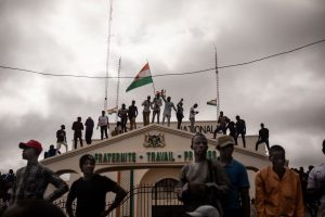 People in Niger stand atop a building, waving the Niger flag, following a coup.