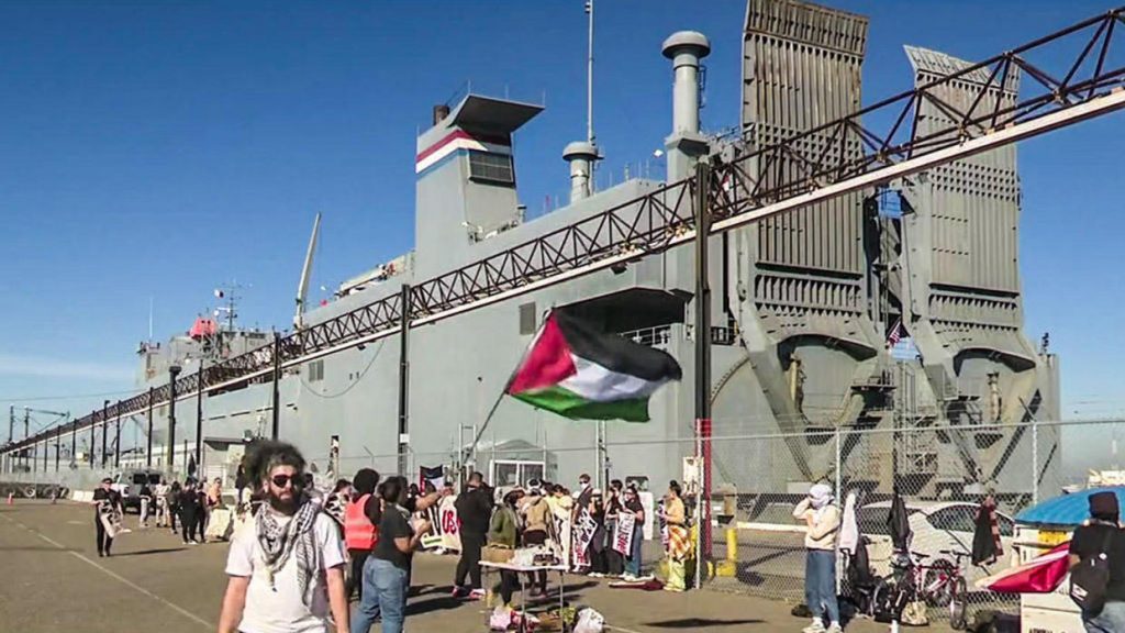 Protesters wave a Palestinian flag in the foreground while blocking a ship in the background