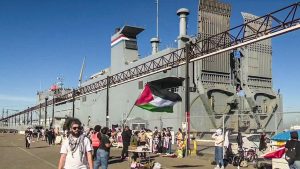Protesters wave a Palestinian flag in the foreground while blocking a ship in the background