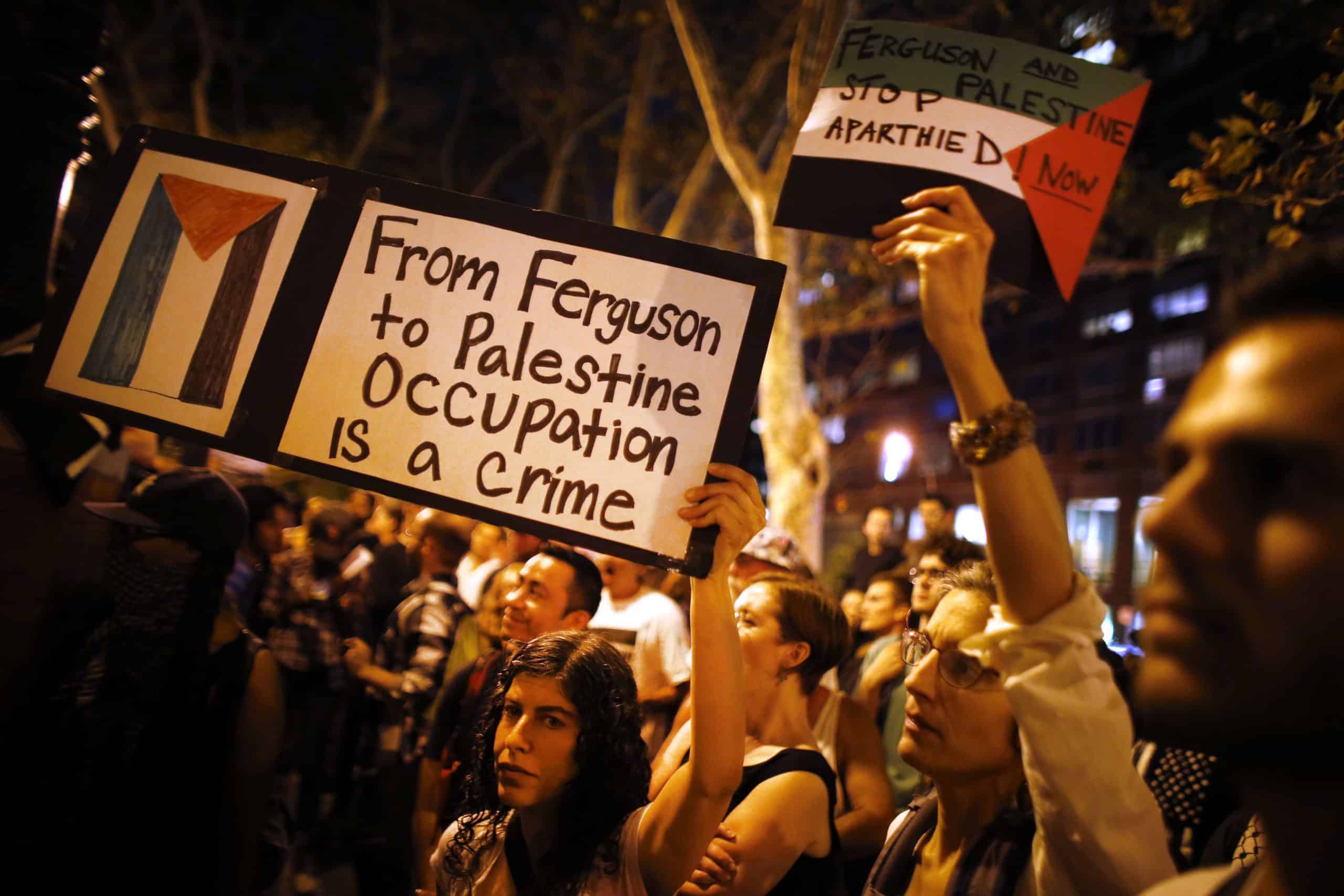 Protesters at an evening protest in NY carry a sign that reads "from ferguson to palestine occupation is a crime"