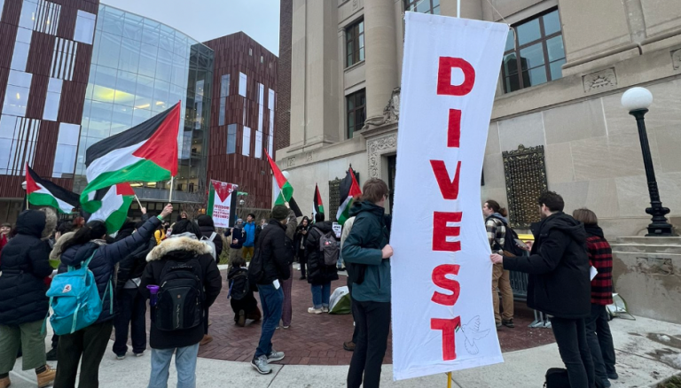 Protesters at the University of Michigan holding Palestine flags and a big banner that reads "DIVEST."