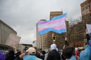A trans flag flies above a protest