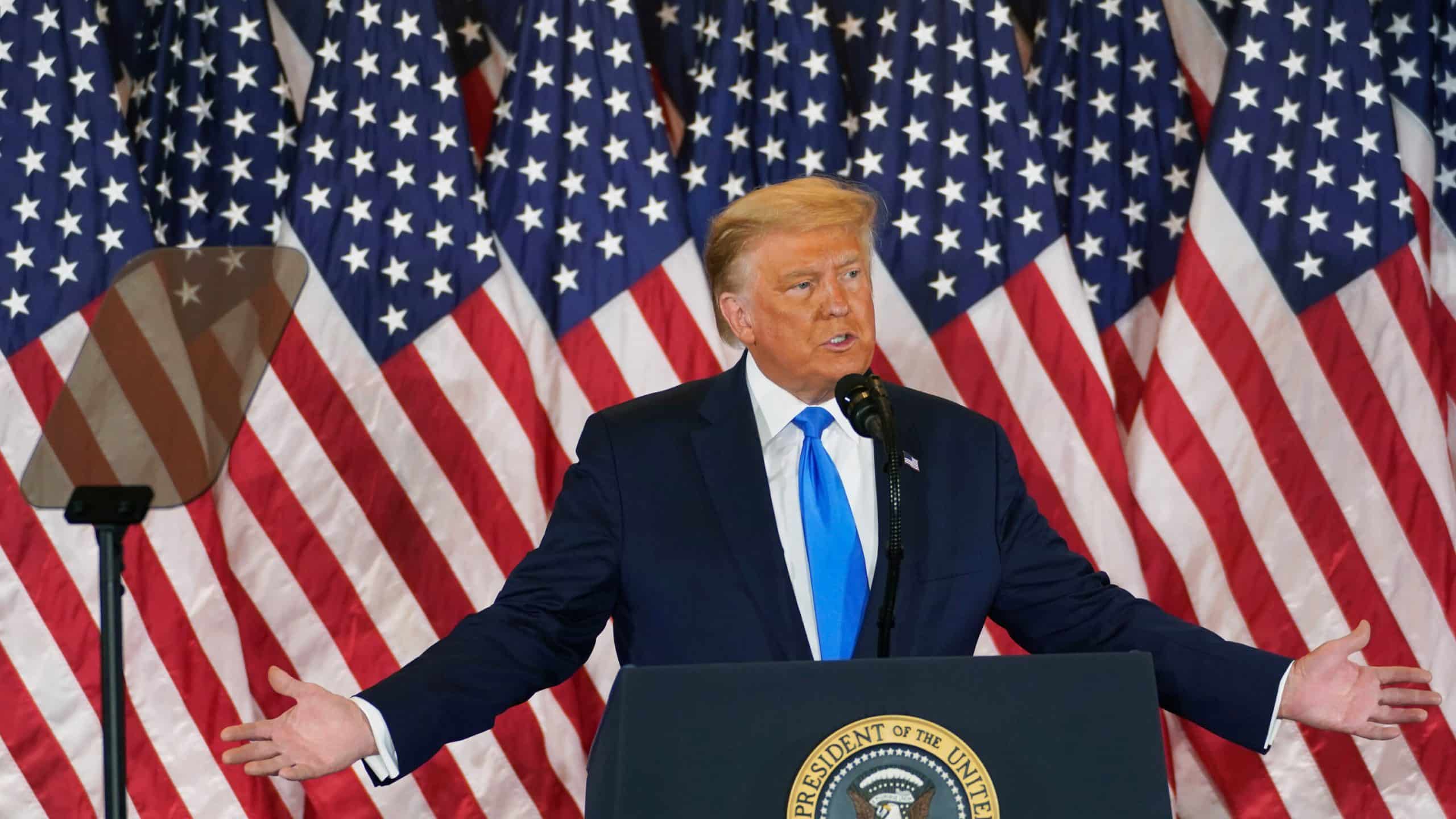 Former president Donald Trump standing at a podium in front of American flags.
