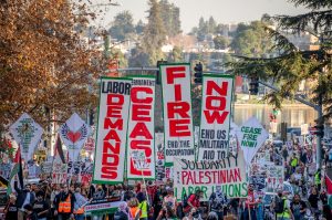 A rally of union members, some hold up a banner that says "Solidarity with Palestinian Labor Unions" others hold up, divided among 4 vertical signs, "Labor Demands Cease Fire Now"