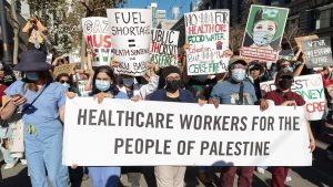 a group of health care workers hold signs including a banner that says "Healthcare workers for the people of Palestine."