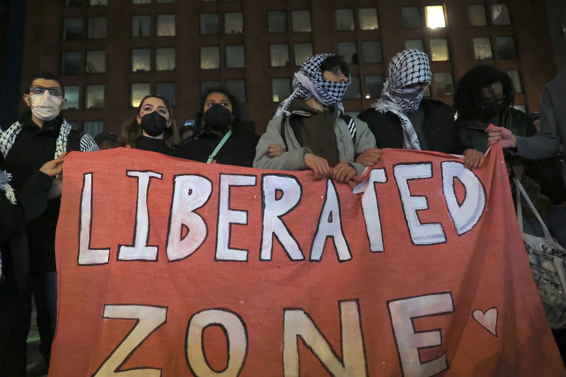 Five masked pro-Palestine protesters hold up a sign that reads "Liberated Zone"