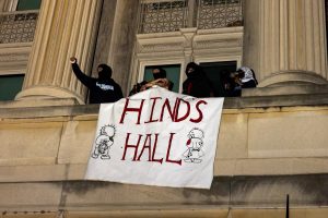 Four masked protesters drop a banner that reads "Hind's Hall" over the balcony of Hamilton Hall at Columbia University