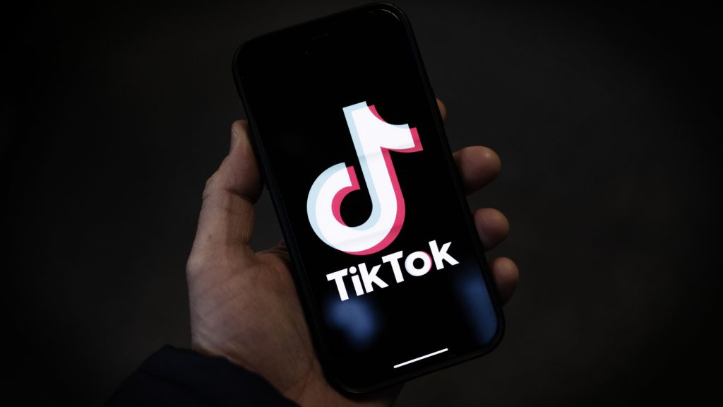 A hand holds a phone which displays the TikTok Logo