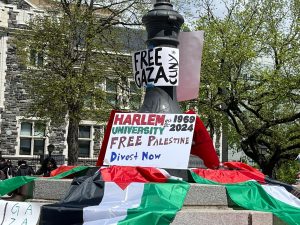 A flagpole in the Gaza Solidarity encampment with Palestine flags, a sign that reads "free gaza, CUNY" and a sign in the center that read "Harlem University, est. 1969, re-est. 2024, Free Palestine, Divest Now"